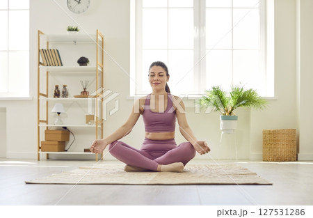 Portrait of a relaxed young woman doing yoga exercise at home sitting in lotus pose. Portrait of a relaxed young woman doing yoga exercise at home sitting in lotus pose. 127531286