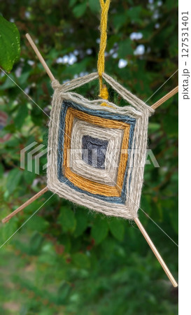 Handmade yarn ornament sways gently in garden tree, handmade details reflect folk roots and mindful art, handmade craft brings cozy spirit to natural surroundings 127531401