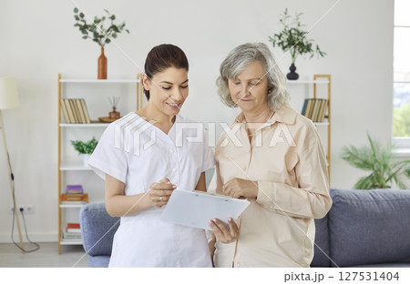Smiling mature woman in nursing home listening to nurse describing treatment plan and providing care Smiling mature woman in nursing home listening to nurse describing treatment plan and providing care 127531404
