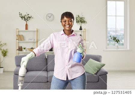 Smiling happy woman holding vacuum cleaner and looking cheerful at camera in living room at home. Smiling happy woman holding vacuum cleaner and looking cheerful at camera in living room at home. 127531405