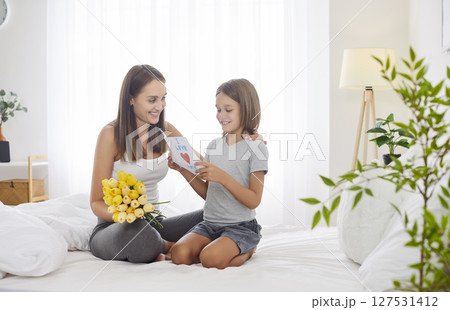 Preteen boy congratulates his mother on holiday by giving her bouquet of yellow tulips and card. 127531412