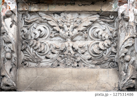 A detailed decorative relief carving on a wall, intricate floral and scroll motifs. Capturing the beauty of historic craftsmanship with an aged and weathered charm, the artistry of the past. 127531486