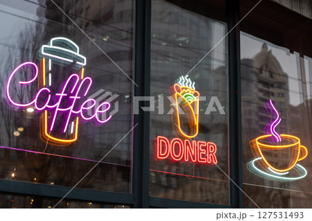 Neon lights featuring coffee, doner kebab, and cup symbols displayed on a glass storefront. These bright signs promote beverages and food, creating a vibrant and welcoming atmosphere for customers. Neon lights featuring coffee, doner kebab, and cup symbols displayed on a glass storefront. These bright signs promote beverages and food, creating a vibrant and welcoming atmosphere for customers. 127531493
