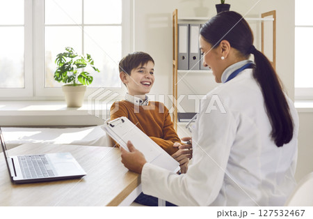 Smiling female pediatrician examining happy preteen boy patient in medical office 127532467