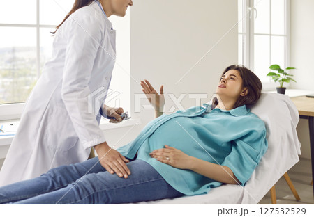 Pregnant woman is talking to female gynecologist doctor during routine checkup at hospital. Pregnant woman is talking to female gynecologist doctor during routine checkup at hospital. 127532529