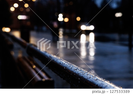 Evening rain brings reflections and lights to the urban street as cars pass by in a tranquil atmosphere Evening rain brings reflections and lights to the urban street as cars pass by in a tranquil atmosphere 127533389