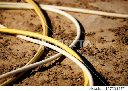 Water hoses intertwined on a sunlit ground during early afternoon outdoor work 127533475