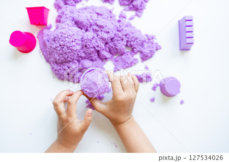 Child hands playing with purple kinetic sand and molds on white background 127534026