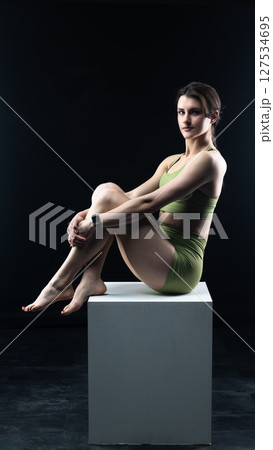 Athletic woman sitting on white cube in sportswear posing on black background 127534695