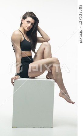 Young athletic woman posing on white cube in studio Young athletic woman posing on white cube in studio 127535308