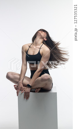 Young athletic woman posing on white cube in studio Young athletic woman posing on white cube in studio 127535321