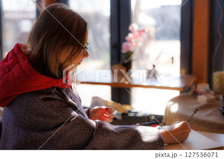 Creative woman sketches meticulously while seated in a cozy cafe during a bright afternoon Creative woman sketches meticulously while seated in a cozy cafe during a bright afternoon 127536071