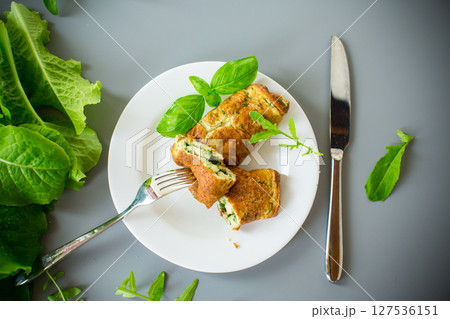Omelette roll with greens on top on a white plate 127536151