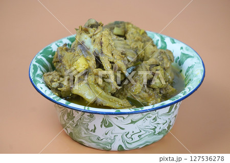 A vibrant bowl of Indonesian soto tulang ayam or chicken bones spicy soup, rich in yellow spices, sits on an orange background 127536278