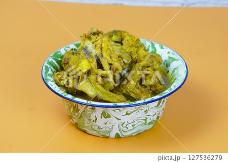 A vibrant bowl of Indonesian soto tulang ayam or chicken bones spicy soup, rich in yellow spices, sits on an orange background 127536279