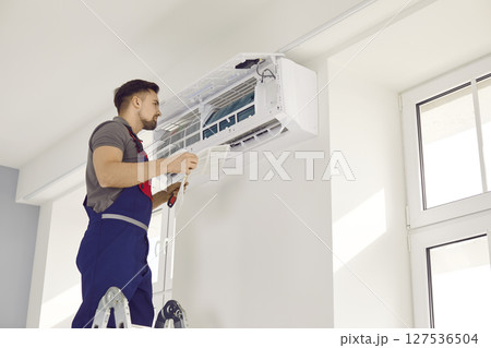 Male technician in uniform repairing air conditioner with screwdriver Male technician in uniform repairing air conditioner with screwdriver 127536504