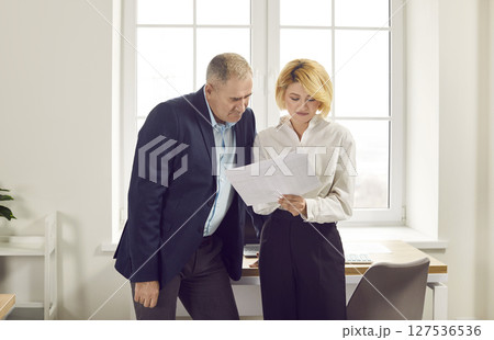 Senior man and young woman standing in the office and reading a business document together 127536536