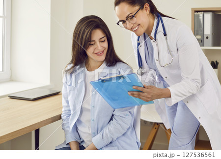Friendly doctor showing report file with appointment to a young pregnant woman. 127536561