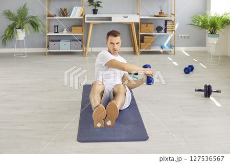 Concentrated athletic man doing exercises with dumbbells during sports training at home. Concentrated athletic man doing exercises with dumbbells during sports training at home. 127536567