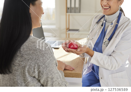 Smiling doctor cardiologist with young happy woman patient on medical examination in clinic. 127536589