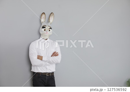 Businessman in a funny rabbit mask standing by a grey copy space wall background 127536592