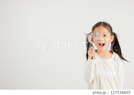 Asian little kid girl funny looking through magnifying glass at studio shot isolated on white background, Happy kindergarten child lifestyle smiling exploring holding magnifier searching, Education 127536605