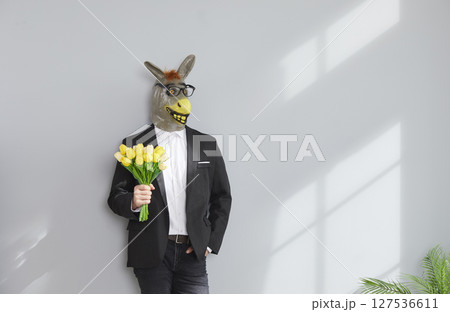Funny man wearing animal donkey mask on head standing with tulip flowers on grey background. 127536611