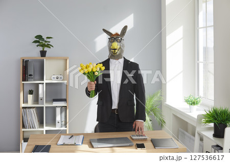 Funny man wearing animal donkey mask on head standing in office with a bouquet of tulip flowers. Funny man wearing animal donkey mask on head standing in office with a bouquet of tulip flowers. 127536617
