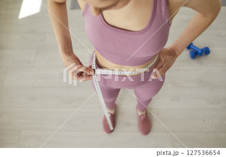 Young woman with beautiful, perfect body measures her waist with centimeter tape 127536654