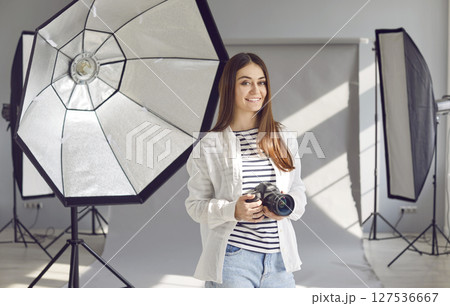 Smiling female photographer standing with professional camera in photo studio 127536667