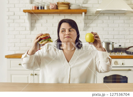 Overweight woman holding apple and burger and choosing between healthy and unhealthy food 127536704