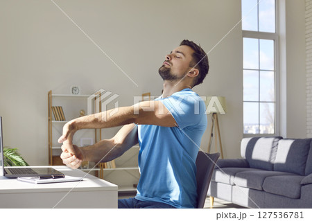 Working man takes a break and does stretching exercise for his arms and shoulders 127536781