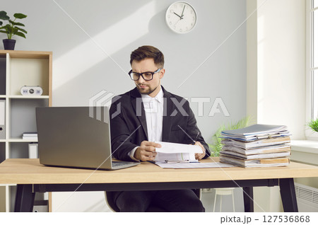 Confident business man working in office with a pile of documents at the desk. 127536868