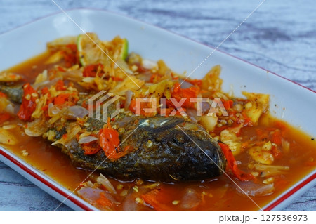 Pecak Ikan Mujair or Fried tilapia doused in a vibrant, spicy, and sour Indonesian chili relish with shallots and lime, served on a white plate. 127536973