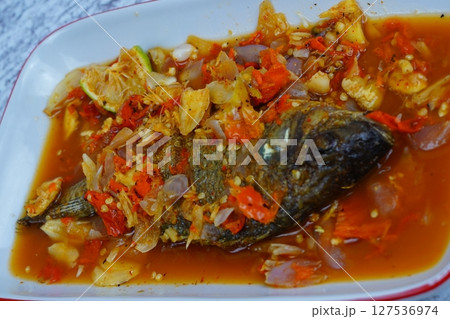 Pecak Ikan Mujair or Fried tilapia doused in a vibrant, spicy, and sour Indonesian chili relish with shallots and lime, served on a white plate. 127536974