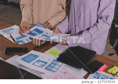 Close up ux developer and ui designer brainstorming about mobile app interface wireframe design on table with customer breif and color code at modern office.Creative digital development agency. Close up ux developer and ui designer brainstorming about mobile app interface wireframe design on table with customer breif and color code at modern office.Creative digital development agency. 127537014