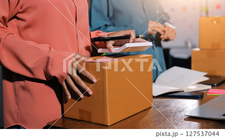 Startup SME small business entrepreneur of freelance Asian woman wearing apron using laptop and box to receive and review orders online to prepare to pack sell to customers, online sme business ideas. Startup SME small business entrepreneur of freelance Asian woman wearing apron using laptop and box to receive and review orders online to prepare to pack sell to customers, online sme business ideas. 127537044