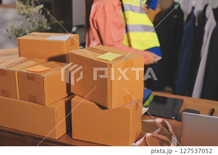 Startup SME small business entrepreneur of freelance Asian woman wearing apron using laptop and box to receive and review orders online to prepare to pack sell to customers, online sme business ideas. 127537052