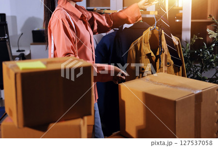 Startup SME small business entrepreneur of freelance Asian woman wearing apron using laptop and box to receive and review orders online to prepare to pack sell to customers, online sme business ideas. 127537058