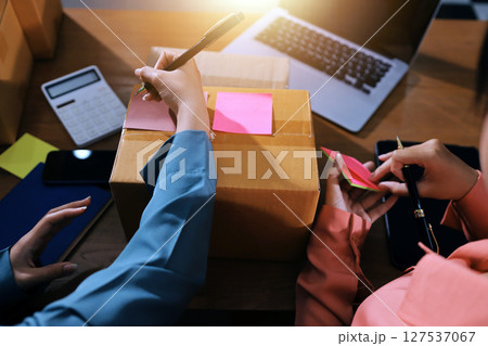 Startup SME small business entrepreneur of freelance Asian woman wearing apron using laptop and box to receive and review orders online to prepare to pack sell to customers, online sme business ideas. 127537067