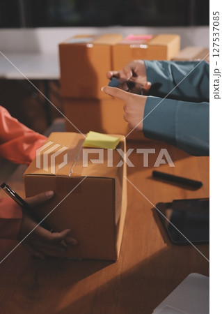 Startup SME small business entrepreneur of freelance Asian woman wearing apron using laptop and box to receive and review orders online to prepare to pack sell to customers, online sme business ideas. 127537085