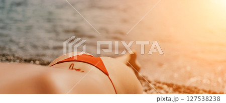 A woman sunbathes on the beach, lying on her stomach in a red swimsuit against the sea backdrop. 127538238