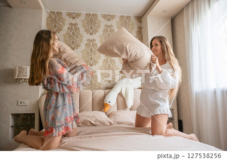Pillow Fight, Bedroom, Fun: Two women playfully fight pillows on bed, home, leisure activity. Pillow Fight, Bedroom, Fun: Two women playfully fight pillows on bed, home, leisure activity. 127538256