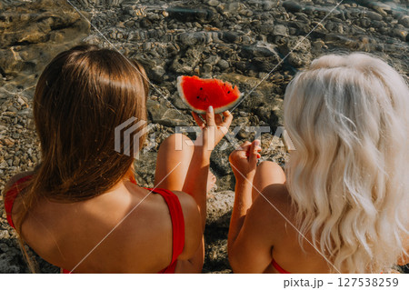Watermelon Beach Summer: Two women enjoy refreshing watermelon slice on rocky seashore during sunny day. Watermelon Beach Summer: Two women enjoy refreshing watermelon slice on rocky seashore during sunny day. 127538259