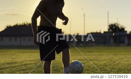 Male feet of professional footballer kicking ball at green field. Legs of young man juggling soccer ball on stadium at sunset. Sportsman practicing tricks outdoor. Freestyle football concept 127538410