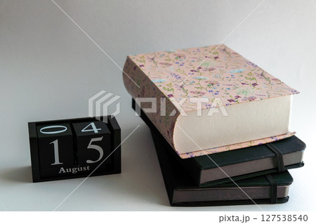Close-up of a stack of textbooks lying on a white background, next to a wooden cube calendar that displays the date "15". The image symbolizes study, education, self-development, planning, and the beg Close-up of a stack of textbooks lying on a white background, next to a wooden cube calendar that displays the date "15". The image symbolizes study, education, self-development, planning, and the beg 127538540