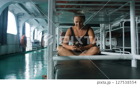 Inside a ferry cabin, a woman relaxes on a bed, scrolling through her phone on the journey Inside a ferry cabin, a woman relaxes on a bed, scrolling through her phone on the journey 127538554