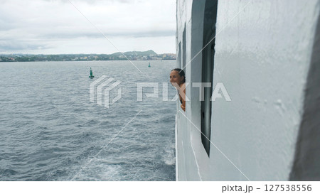 Wind tousles a young woman's hair as she leans out the ferry window, enjoying the view 127538556