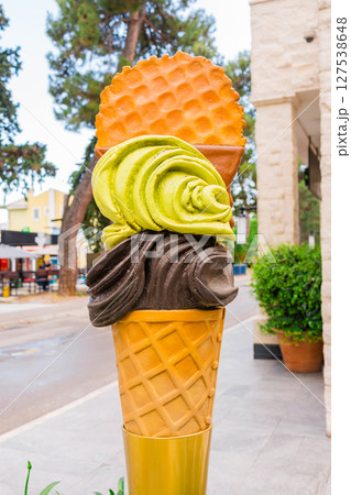 Colorful giant ice cream cone statue with pistachio and chocolate scoops. Street decoration in a seaside town evoking summer mood and playful charm. 127538648