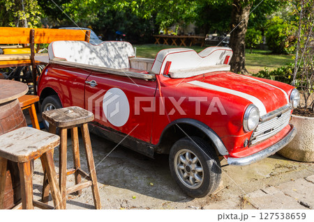 Retro red convertible car repurposed as outdoor seating. Vintage automotive decor, upcycled design and quirky cafe atmosphere. 127538659